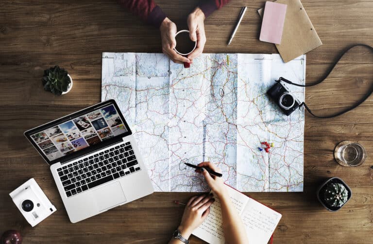 A travel map, camera and notebook laid out on a desk for trip planning